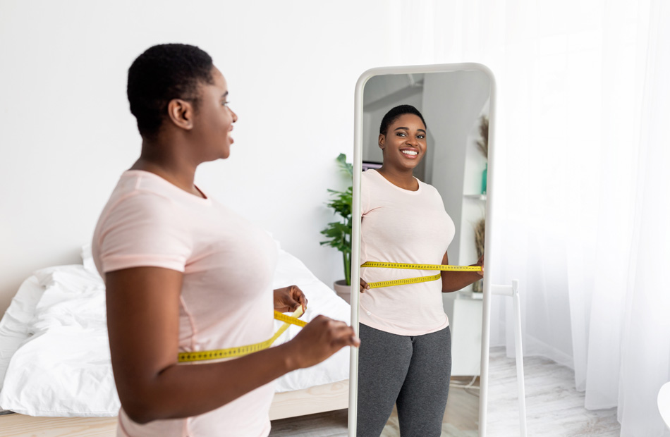 Woman measuring waist in bedroom mirror
